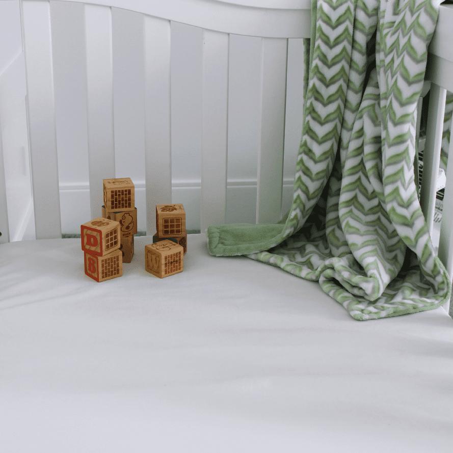 SaniSnooze Waterproof Crib Mattress in a white crib with blocks and blanket